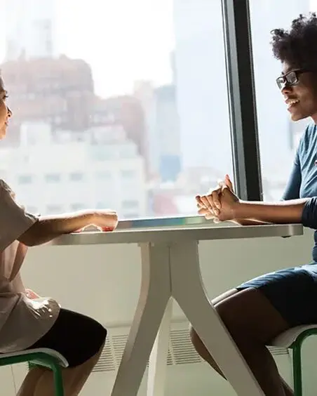 Two women sitting at a table with cups of coffee.